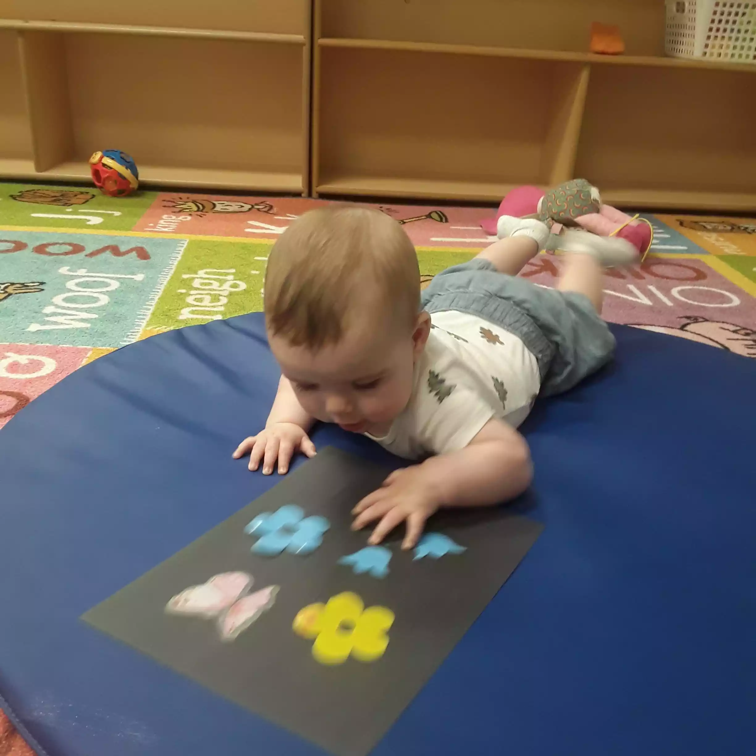 Infant Exploring Spring Flower and Butterfly Cutouts During Tummy Time - Pinebrook- Preschool - Pinebrook- Preschool Infant during tummy time sensory activity in daycare classroom