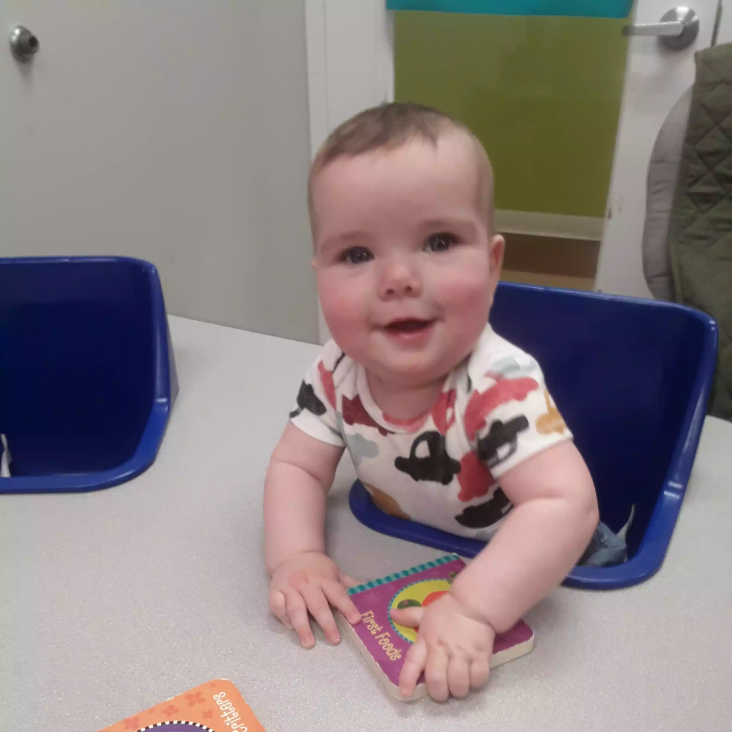 Infant Reading Board Books at the Activity Table - Pinebrook- Preschool - Pinebrook- Preschool Baby sitting at table with board books in infant program