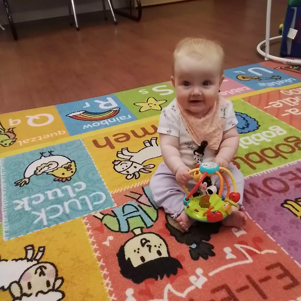 Baby sitting on colorful play mat with interactive sensory rattle in infant program