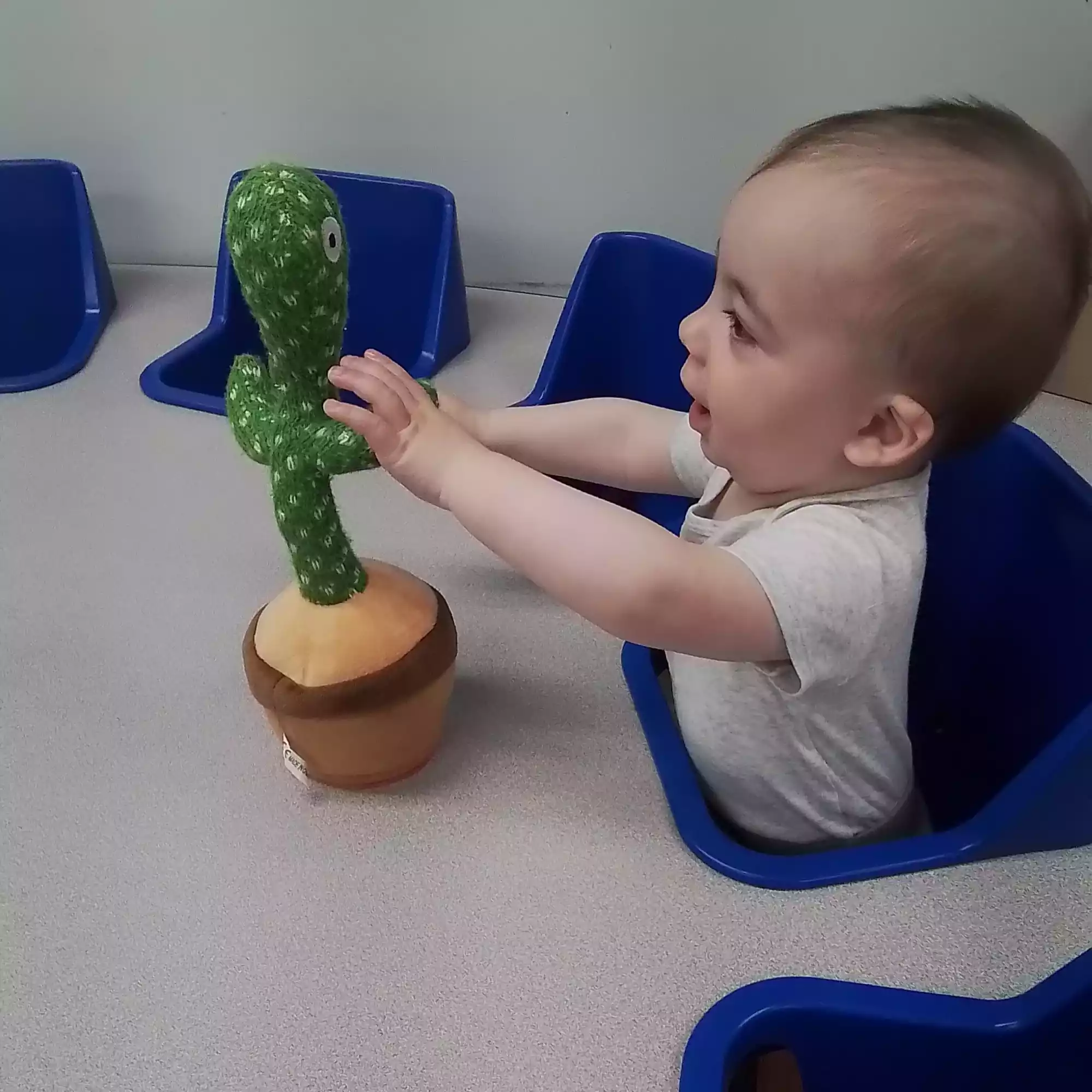 Infant Reaching for Interactive Dancing Cactus Toy - Pinebrook- Preschool - Pinebrook- Preschool Infant reaching for dancing cactus sensory toy at activity table in daycare