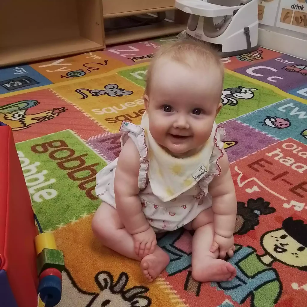 Infant practicing sitting skills on alphabet rug in daycare classroom