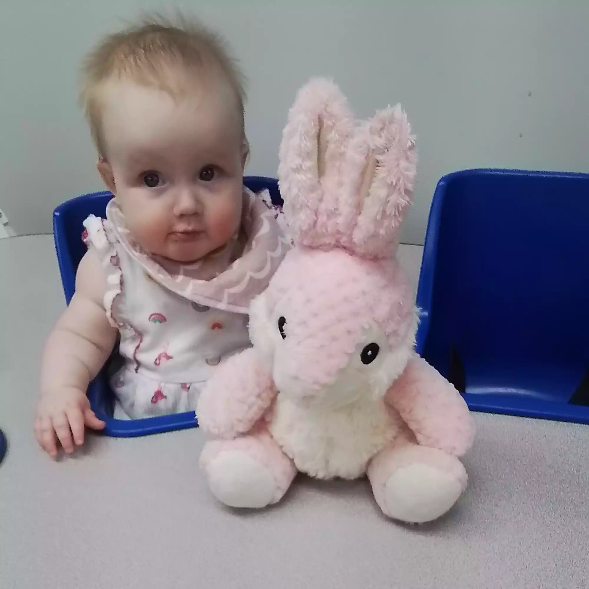 Infant Exploring Plush Bunny Toy - Pinebrook- Preschool - Pinebrook- Preschool Infant seated with plush bunny toy during sensory play in daycare classroom