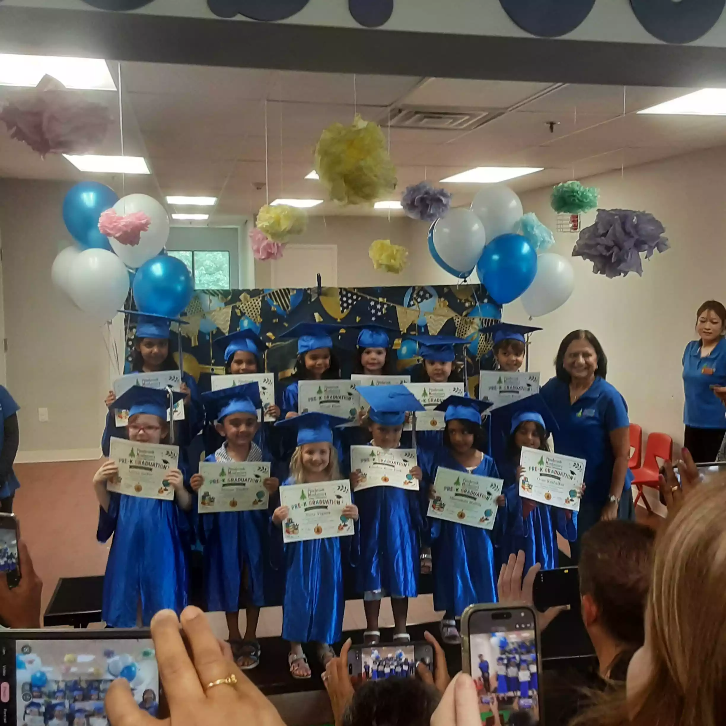Audience Photographing Pinebrook Graduation Class - Pinebrook- Preschool - Pinebrook- Preschool Audience holding smartphones to photograph pre-K graduation group