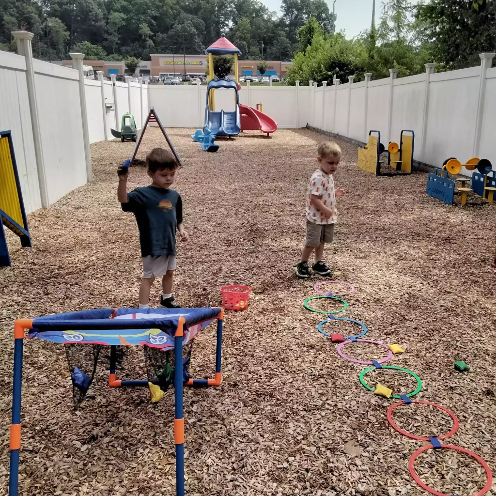 Two boys taking turns throwing beanbags at a target on a woodchip playground.
