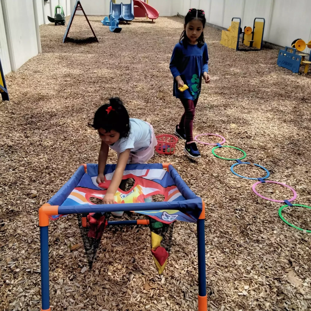 A young girl reaching into a net target during an outdoor lawn game while another girl walks nearby.