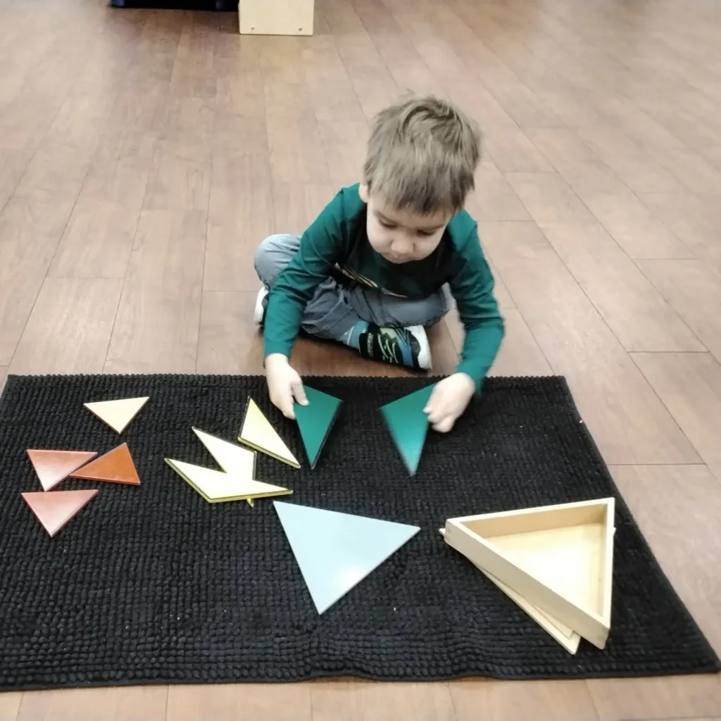 Young child sitting on a black rug, arranging colorful wooden triangles into shapes.