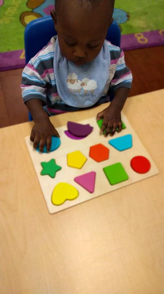 Young child sits at a table placing colorful shapes into a puzzle board.
