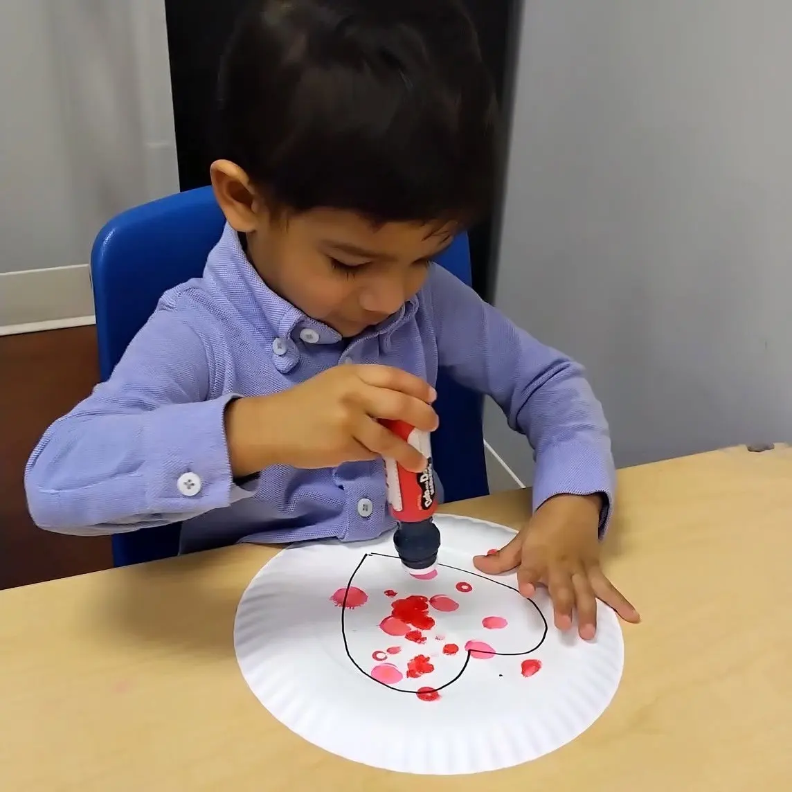 Two children sit at a table cutting out shapes from paper with scissors during a craft activity in a classroom.