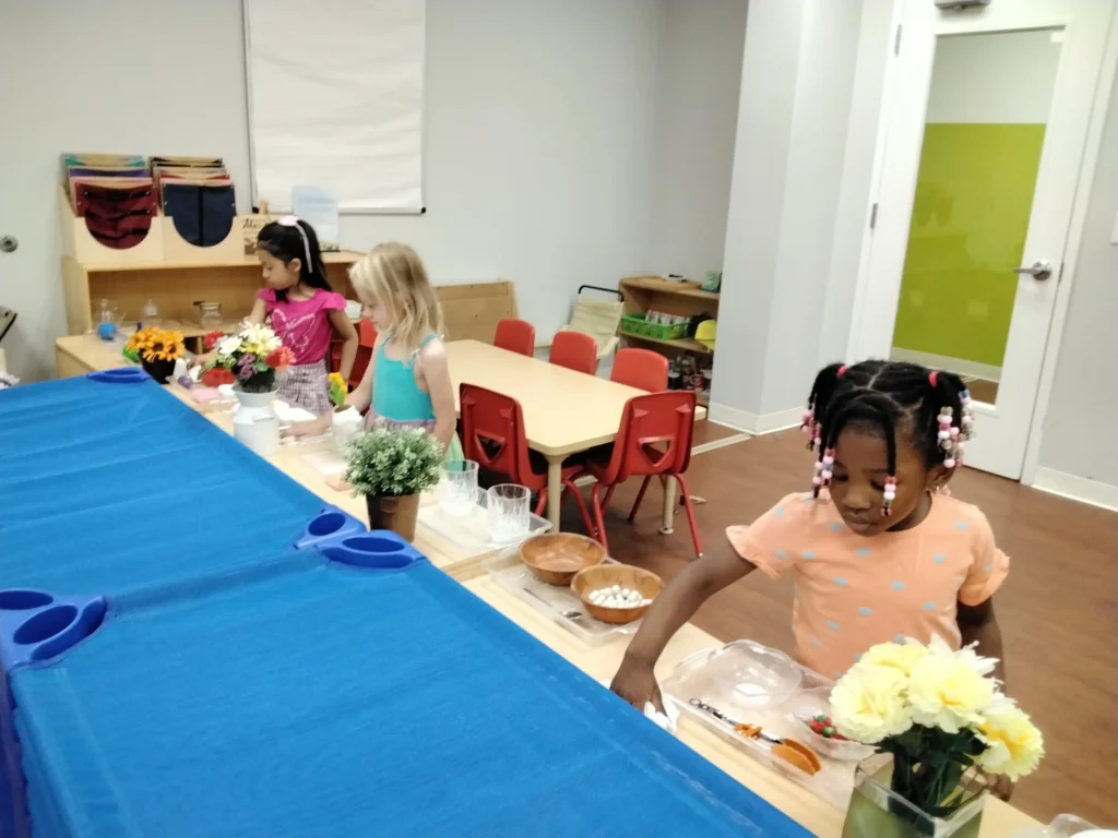 Children sit at a classroom craft table making flower arrangements with colorful blooms and supplies nearby nearby.